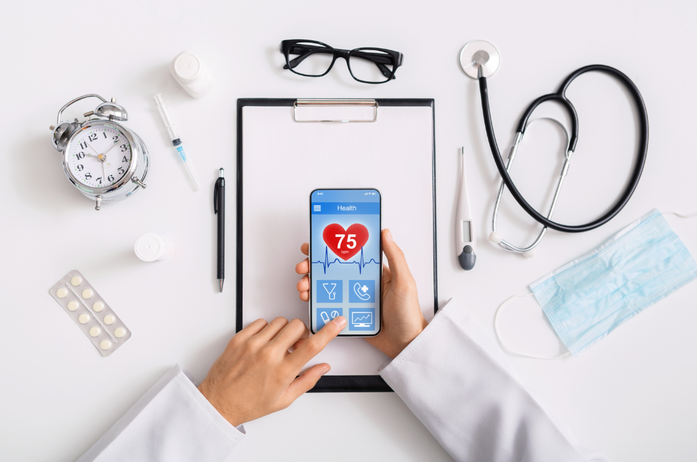 A flat lay of medical tools including a stethoscope, thermometer, and a smartphone displaying a health app with a heartbeat graphic and a heart rate of 75.