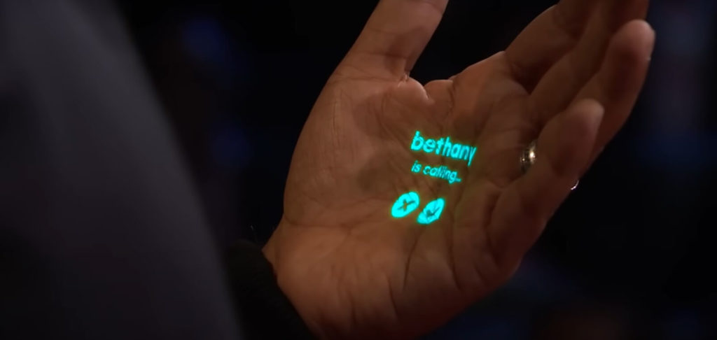 A person's open hand with a projected holographic display showing an incoming call from "bethany," with call accept and decline icons.